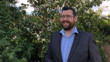 Peter Rowletter standing of front of a green, leafy bush.