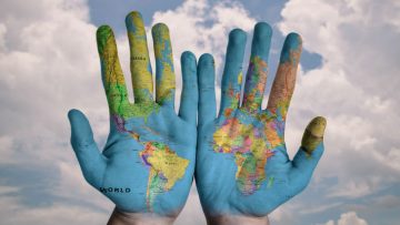 A-person's-palms-with-a-world-map-painted-on-them-held-up-against-a-cloudy-sky