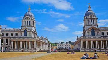 a photo of Greenwich University with a background of blue sky. A grassed area is in the foreground, with some people sitting together in small groups on it.