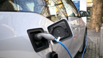 Side view of a white car, it is plugged in to charge via a blue cable.