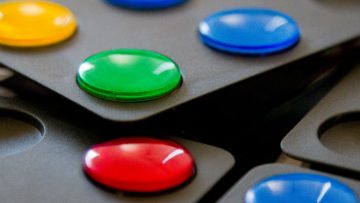 A close-up view of Pentago game discs in red, blue, yellow and green on black game boards
