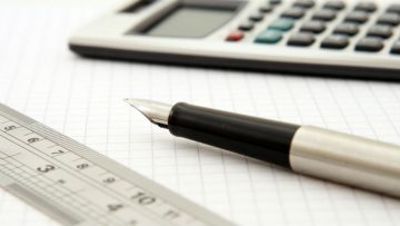 A metal ruler, fountain pen and calculator on top of squared paper.