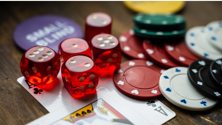 A close-up shot of red dice, multicoloured gambling chips and two playing cards on a dark wooden table.