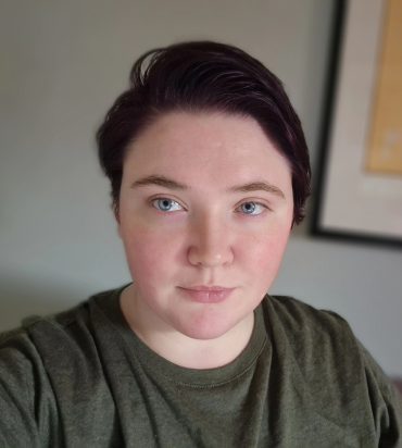 A portrait of Elysia Barker, a white woman with short chestnute brown hair, wearing a khaki green shirt