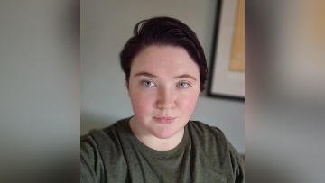 A portrait of Elysia Barker, a white woman with short chestnute brown hair, wearing a khaki green shirt