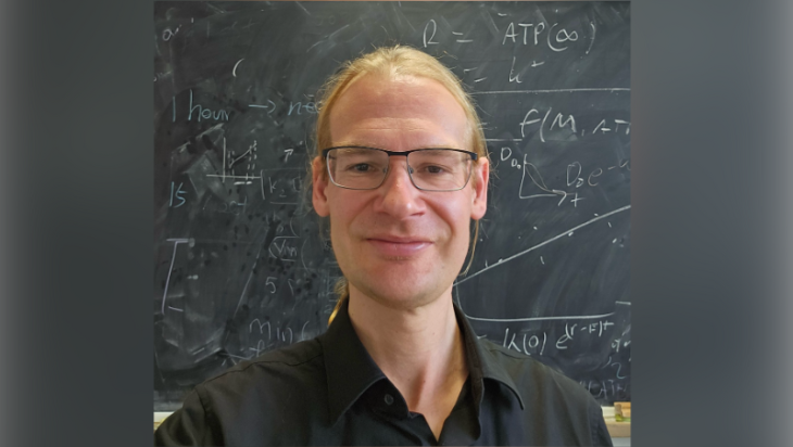 Headshot of Fabian Spill standing in front of a chalk board